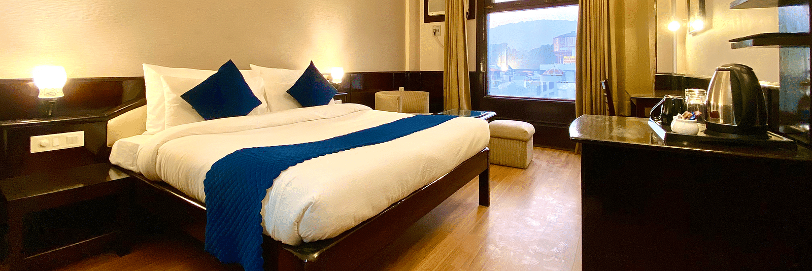 A hotel room with a king size bed, a desk, a chair, a flat-screen TV, and a window with a view of a lake  | DLS Park Grace, Haridwar